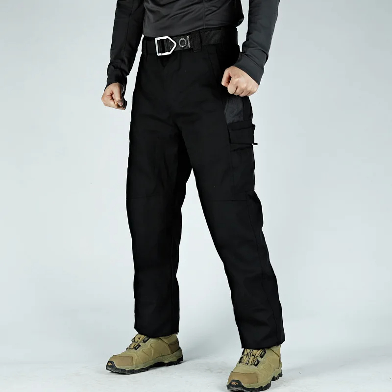 Model wearing durable black trekking trousers with multi-pockets, reinforced knees, and tactical design, perfect for outdoor adventures.